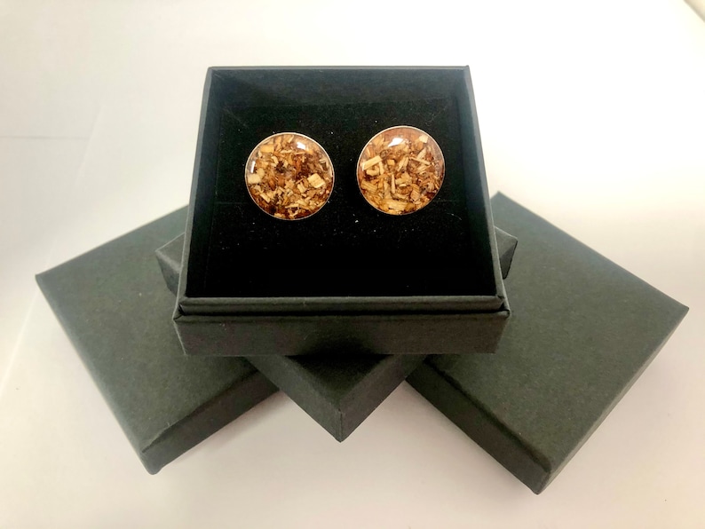 May include: A pair of round wood-filled resin earrings in a black gift box. The earrings are a light brown color with flecks of gold.