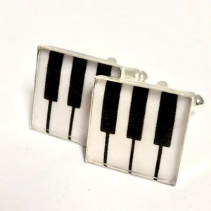 May include: A pair of silver cufflinks with a black and white piano key design.