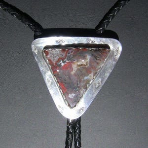 May include: A silver bolo tie with a triangular pendant featuring a red, brown, and white agate stone.
