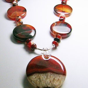 May include: A necklace featuring a large, circular, polished red and white agate pendant suspended from a silver-toned bail. The chain consists of alternating smooth, round, translucent red and brown agate discs and smaller spherical beads.
