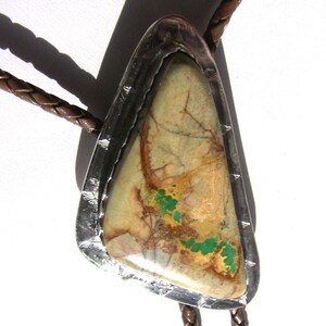 May include: A bolo tie with a silver setting and a large, triangular, green and brown stone.