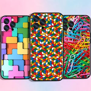 May include: Three phone cases with colorful designs. One case features a Tetris-like pattern in various colors. Another has a geometric cube pattern in red, yellow, blue, and green. The third case is covered in colorful paperclips.