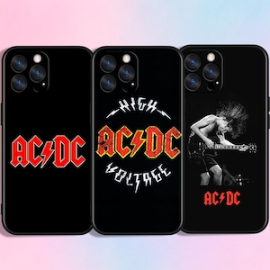 Op de afbeelding: Zwarte telefoonhoesjes met AC/DC-ontwerpen. Eén hoesje toont het AC/DC-logo in rood, een ander "HIGH VOLTAGE" en de derde een gitarist en het AC/DC-logo in rood.