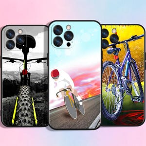 Op de afbeelding: Drie smartphonehoesjes met fietsthema's. Het linkerhoesje toont een zwart-wit achteraanzicht van een mountainbike. Het middelste hoesje toont een fietser op een weg bij zonsondergang. Het rechterhoesje toont een paarse fiets op een achtergrond.
