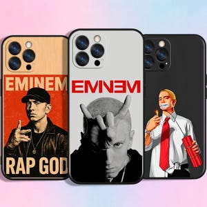 May include: Three phone cases featuring rapper Eminem. One case has a wooden texture with the text "EMINEM" and "RAP GOD". Another case has a black and white image of Eminem with the text "EMINEM" in red. The third case has a black background with an image of Eminem.