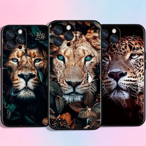 Op de afbeelding: Drie smartphonehoesjes met hoge resolutie dierenportretten. Het linkerhoesje toont een leeuw in donker gebladerte, het middelste hoesje een leeuw met helderblauwe ogen tussen bladeren en het rechterhoesje een luipaard met intense ogen.