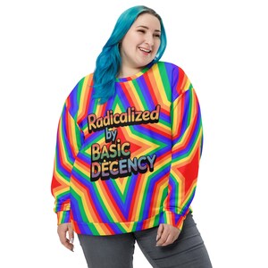 Puede incluir: Una sudadera vibrante a rayas de arcoíris con el texto "Radicalized by Basic Decency" en una fuente colorida y delineada. La sudadera presenta un patrón geométrico y la lleva una persona con cabello azul.