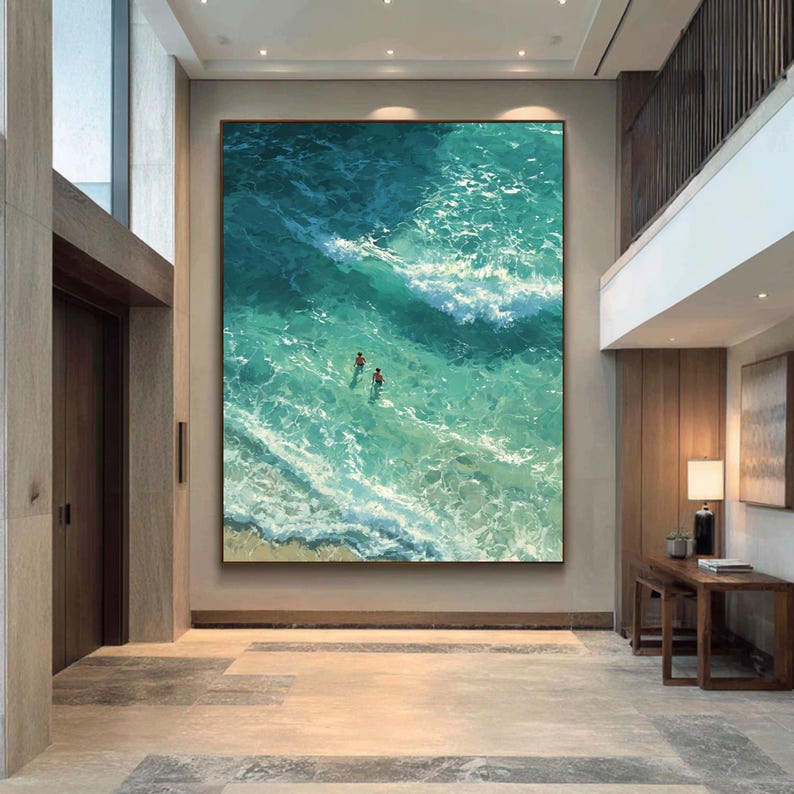 Puede incluir: Obra de arte enmarcada de gran tama&ntilde;o que representa una vista a&eacute;rea de las olas turquesas del oc&eacute;ano. Dos figuras nadan en el agua. La pintura se exhibe en un pasillo moderno y bien iluminado.