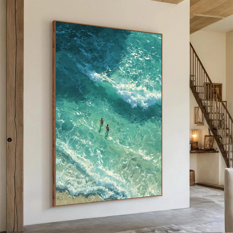 Puede incluir: Gran obra de arte enmarcada que representa a dos figuras nadando en agua de mar turquesa. La pintura presenta olas blancas y una orilla arenosa, con un marco de madera. La obra de arte se exhibe en una pared blanca.