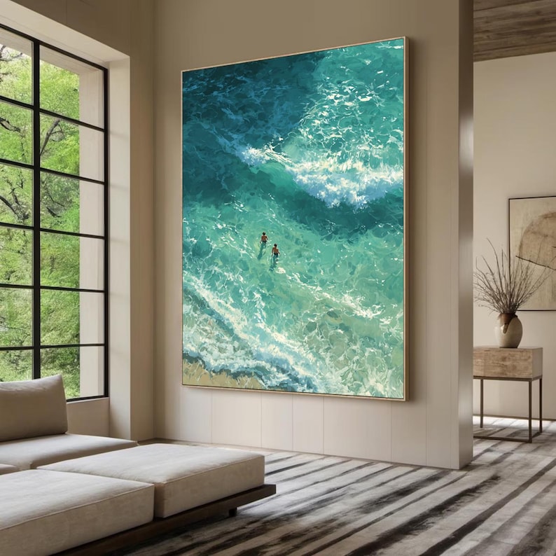 Puede incluir: Gran obra de arte enmarcada que representa una vista a&eacute;rea del oc&eacute;ano. La pintura presenta olas turquesas y blancas, con dos peque&ntilde;as figuras nadando cerca de la orilla. La obra de arte se exhibe en un sal&oacute;n moderno.