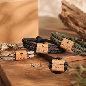 May include: Three paracord bracelets featuring wooden beads engraved with a cross and names Aiden, Elijah, and Benjamin. A circular inset shows the back of a bead with the text CONFIRMATION and 02.03.2026. The bracelets use black, olive, and tan cord.