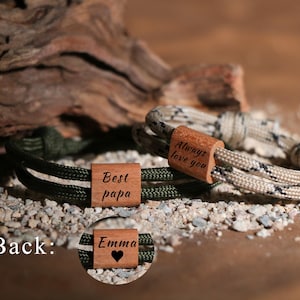 May include: Two handmade bracelets with wooden accents. One bracelet is olive green and black, the other is beige and black. The wooden accents are engraved with the phrases "Best papa" and "Always love you". A third wooden accent is engraved with "Emma" and a heart.