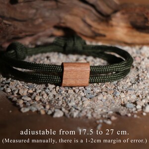 May include: An olive green rope bracelet with a wooden rectangular clasp. The bracelet is adjustable from 17.5 to 27 cm. The text on the image says "adiustable from 17.5 to 27 cm."