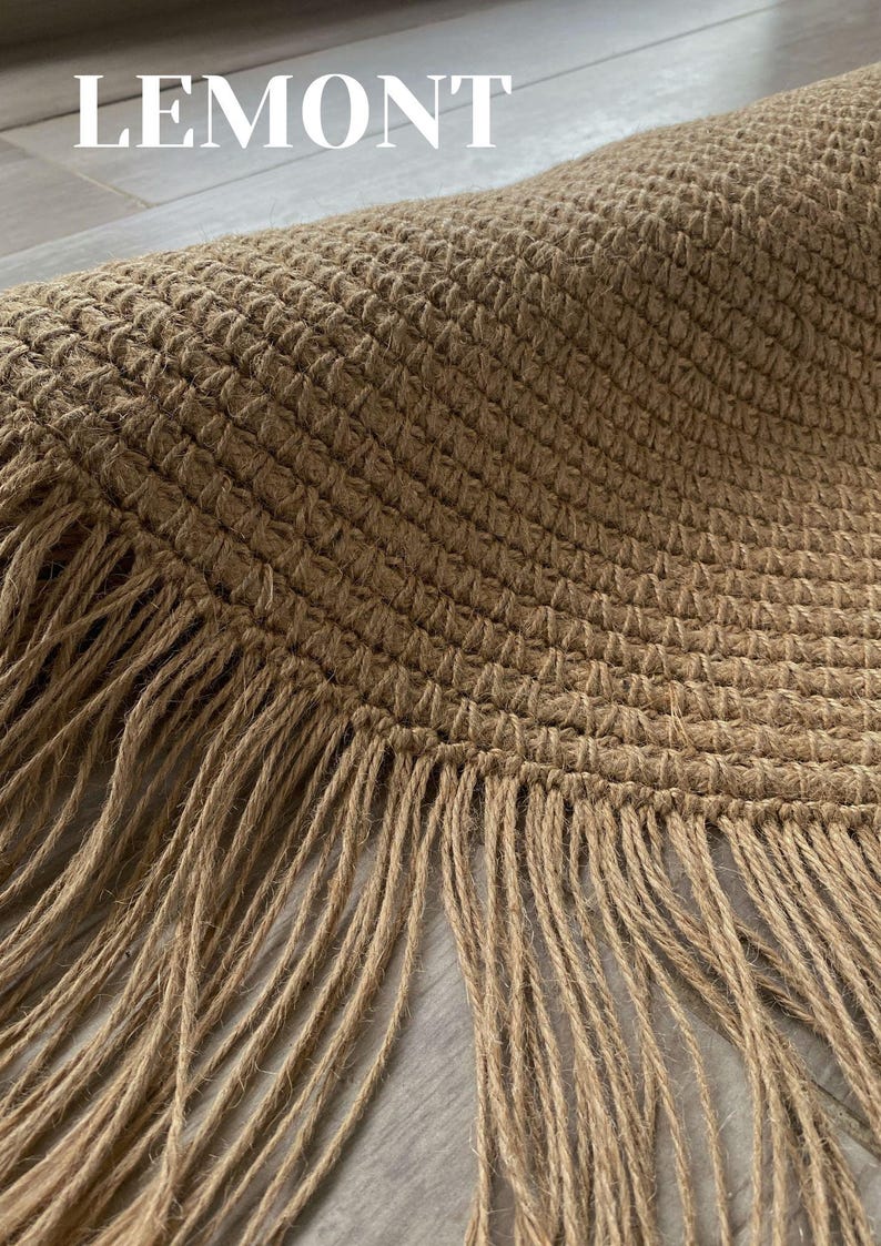 K&ouml;nnte beinhalten: Nahaufnahme eines runden, gewebten Jute-Teppichs mit Fransenrand. Der Teppich hat eine nat&uuml;rliche beige Farbe und eine strukturierte Oberfl&auml;che. Das Wort "LEMONT" ist oben im Bild wei&szlig; gedruckt.