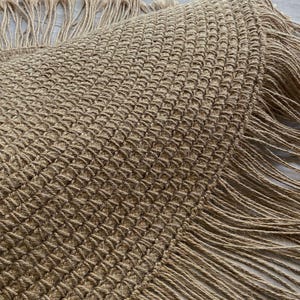 K&ouml;nnte beinhalten: Ein runder, gewebter Jute-Teppich mit strukturiertem Muster und Fransen. Der Teppich hat eine nat&uuml;rliche beige Farbe und tr&auml;gt oben das Wort "LEMONT" in wei&szlig;en Blockbuchstaben. Geeignet f&uuml;r die Inneneinrichtung.