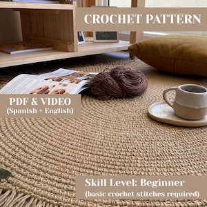 Könnte beinhalten: Ein runder, beigefarbener Häkelteppich mit Fransen. Das Bild enthält den Text "CROCHET PATTERN", "PDF & VIDEO (Spanisch + Englisch)" und "Skill Level: Beginner (basic crochet stitches required)". Eine Tasse und Untertasse liegen auf dem Teppich.
