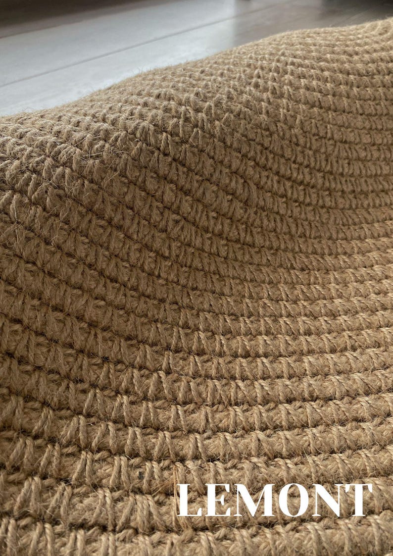 K&ouml;nnte beinhalten: Nahaufnahme eines gewebten, braunen Teppichs mit strukturierter Oberfl&auml;che. Der Teppich besteht aus Naturfasern und hat ein sich wiederholendes Muster. Das Wort "LEMONT" ist unten auf dem Teppich wei&szlig; gedruckt.