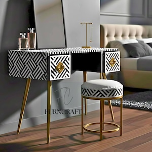 May include: A black and white patterned vanity table with gold legs and drawer pulls. A matching stool sits in front of the table. A mirror and perfume bottles are on the table. The room has a bed in the background.
