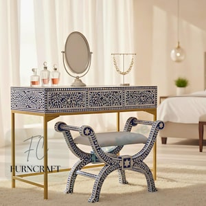 May include: A vanity set with a navy blue and white floral design. The set includes a vanity table with three drawers, a matching stool, and a round mirror. The table has a gold metal frame. Perfume bottles and a necklace holder are on the table.