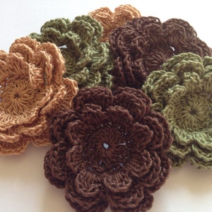May include: Five crocheted flowers in shades of brown, green, and beige. The flowers are layered and have a delicate, intricate design.