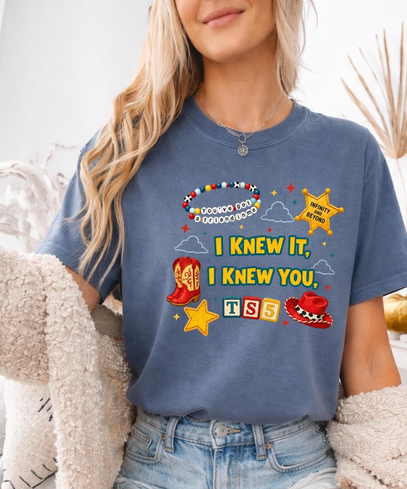 K&ouml;nnte beinhalten: Ein blaues T-Shirt mit einem Grafikdruck, der ein Perlenarmband mit der Aufschrift You've got a friend in me, einen gelben Sheriffstern, rote Cowboystiefel, einen roten Cowboyhut, TS5-Bl&ouml;cke und den Text I KNEW IT, I KNEW YOU zeigt.