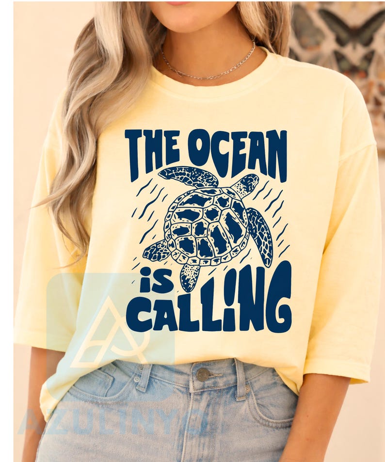 K&ouml;nnte beinhalten: Ein hellgelbes T-Shirt mit kurzen &Auml;rmeln und einer dunkelblauen Grafik einer Meeresschildkr&ouml;te auf der Brust. Der Text &uuml;ber und unter der Schildkr&ouml;te lautet THE OCEAN is CALLING in einer fetten, dunkelblauen Schrift. Rundhalsausschnitt.