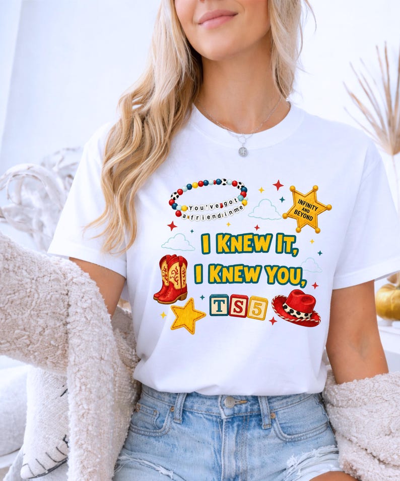 K&ouml;nnte beinhalten: Ein wei&szlig;es kurz&auml;rmeliges T-Shirt mit einem bunten Grafikdruck. Das Design zeigt ein Perlenarmband mit dem Text 'You've got a friend in me', einen gelben Sheriffstern, rote Cowboystiefel, einen roten Cowboyhut und Spielw&uuml;rfel mit der Aufschrift 'TS5'.
