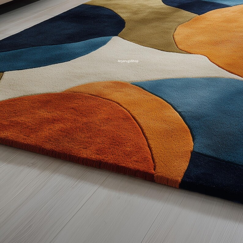 May include: A colorful area rug with an abstract design. The rug features large, irregular shapes in shades of orange, blue, beige, and olive green. The texture appears plush and soft, with a close-up view highlighting the detailed craftsmanship.