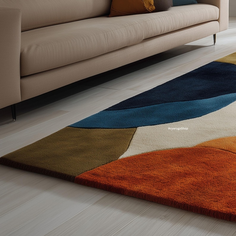May include: A rectangular area rug with an abstract design in shades of blue, brown, orange, and white. The rug is placed on a light-colored wooden floor, partially under a beige sofa.