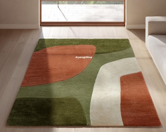 May include: A rectangular area rug featuring an abstract pattern of large, organic shapes in shades of olive green, burnt orange, and cream. The rug has a textured pile surface and includes the text AryarugsShop printed in the center.