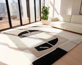 Puede incluir: Una alfombra moderna con un diseño geométrico. La alfombra presenta una combinación de formas rectangulares y semicirculares negras, blancas y beige. Está colocada sobre un suelo de madera clara en una habitación luminosa.