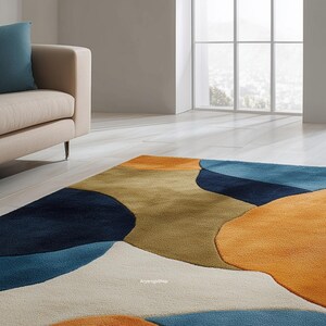 May include: A colorful area rug with an abstract design. The rug features large, irregular shapes in shades of navy blue, orange, tan, and light blue against a cream background. The rug is placed on a light wood floor, with a beige sofa and window in the background.