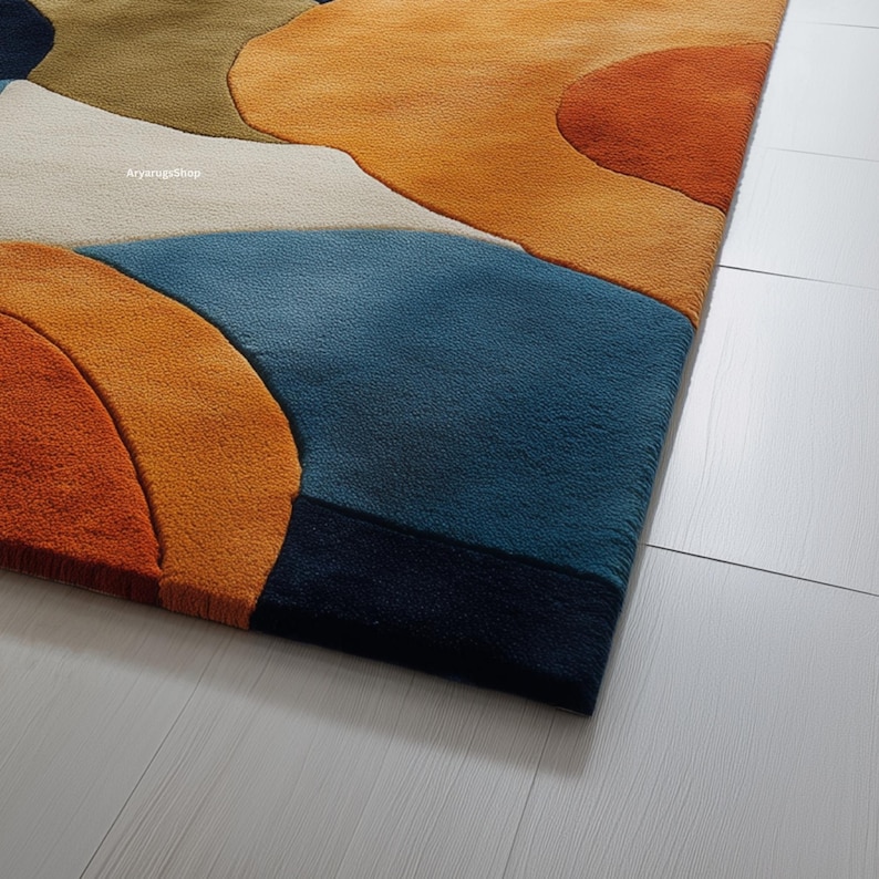 May include: A colorful area rug with an abstract design. The rug features a combination of orange, blue, white, and green shapes. The rug's texture is visible, and the design is modern and eye-catching.
