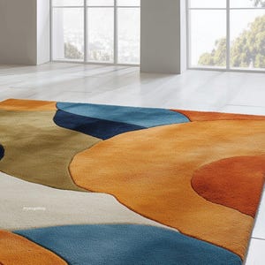 May include: A colorful area rug with an abstract design. The rug features large, flowing shapes in shades of orange, blue, tan, and white. The rug is made of a soft material and is suitable for a living room or bedroom.