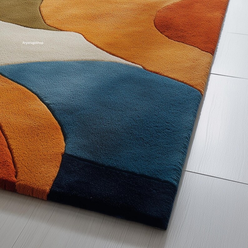 May include: Close-up of a colorful area rug with an abstract design. The rug features a combination of orange, blue, cream, and brown hues. The rug's texture is visible, and the design is reminiscent of a landscape.