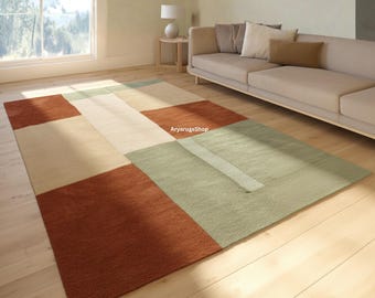 Puede incluir: Una alfombra rectangular con un patrón geométrico de bloques de color en tonos terracota, verde salvia y crema. La alfombra presenta un diseño a gran escala con secciones rectangulares de color sólido e incluye el texto AryarugsShop.