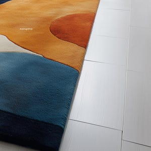 May include: A close-up of a colorful area rug with an abstract design. The rug features a combination of blue, orange, and cream colors. The rug is placed next to a white wooden floor.