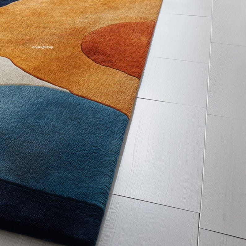 May include: A close-up of a colorful area rug with an abstract design. The rug features a combination of blue, orange, and cream colors. The rug is placed next to a white wooden floor.