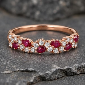 Puede incluir: Un anillo de oro rosa con una banda delicada engastada con rubíes rojos de talla marquesa y pequeños diamantes blancos redondos alternados. Las piedras están dispuestas en un patrón continuo y repetitivo en la parte frontal del anillo.