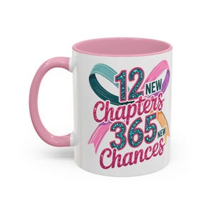 Könnte beinhalten: Weißer Keramikbecher mit rosa Innenraum und Henkel. Der Becher zeigt den Text "12 New Chapters 365 New Chances" in einem farbenfrohen, glitzernden Design mit türkisfarbenen, rosa und orangefarbenen Bändern. Ein motivierendes Geschenk.