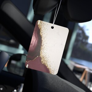 以下が含まれることがあります： ボルドーと白のマーブル模様に金色のグリッターがアクセントになった、長方形の車用芳香剤。白い紐で吊り下げられており、車内に吊るすようにデザインされています。