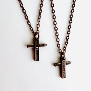 May include: Two copper chain necklaces with cross pendants. The cross on the left is plain, while the cross on the right has the words "Ground Zero Rebuilt" engraved on it.