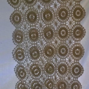 May include: A delicate crocheted tablecloth with a pattern of repeating circles and flowers. The tablecloth is made of a light beige yarn and has a scalloped edge.