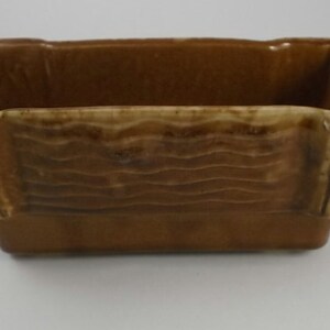 May include: A brown ceramic planter with a wavy design and a rectangular shape. The planter has a light brown glaze and a slightly raised rim.
