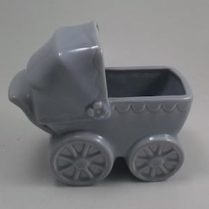 May include: A light blue ceramic baby carriage planter. The carriage has a white scalloped trim and a white flower detail on the hood.