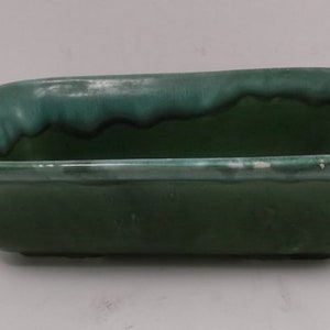 May include: A rectangular green ceramic planter with a glazed finish. The planter has a slightly raised rim and a smooth, even surface.