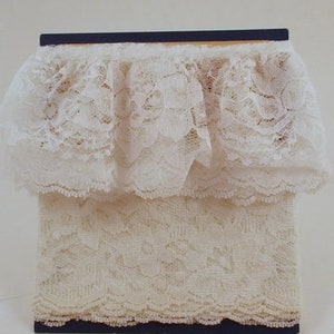 May include: Two pieces of white lace trim, one with a ruffled edge and the other with a scalloped edge. The lace is displayed on a black card.