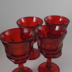 May include: Set of four red glass wine goblets with a textured design. The goblets have a round bowl and a tall stem.