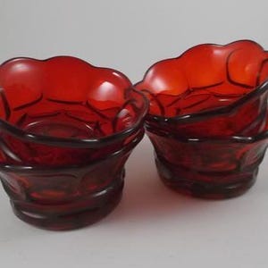 May include: Set of four red glass bowls with a scalloped rim and a textured design. The bowls are stacked on top of each other.