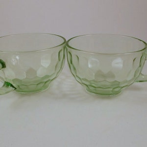 Puede incluir: Dos tazas de vidrio verde con un diseño texturizado y burbujeante. Las tazas tienen una forma redondeada y un asa.